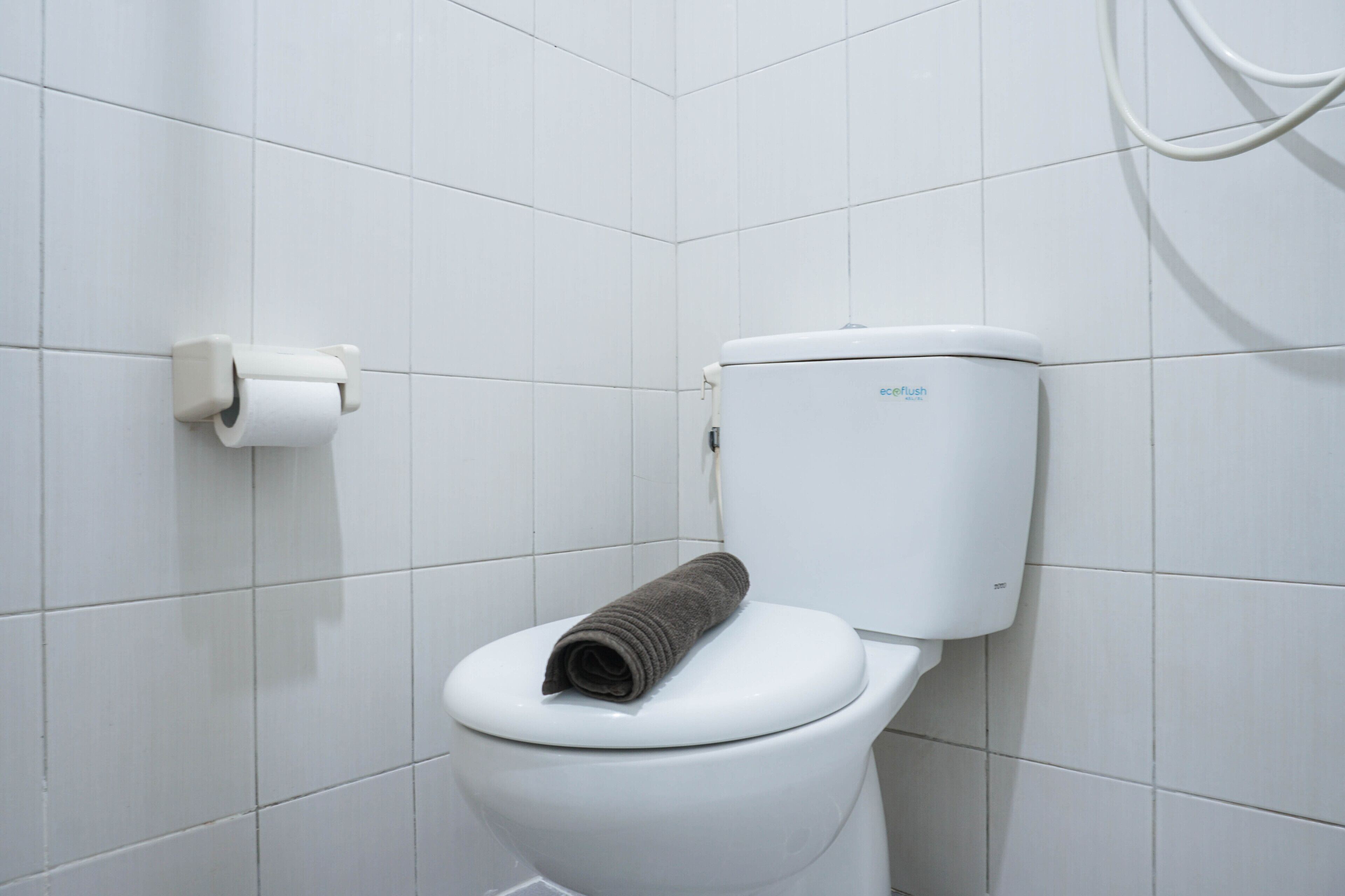 Eine weiße Toilette mit einem Handtuch auf dem Sitz und einem Toilettenpapierhalter an der Wand.