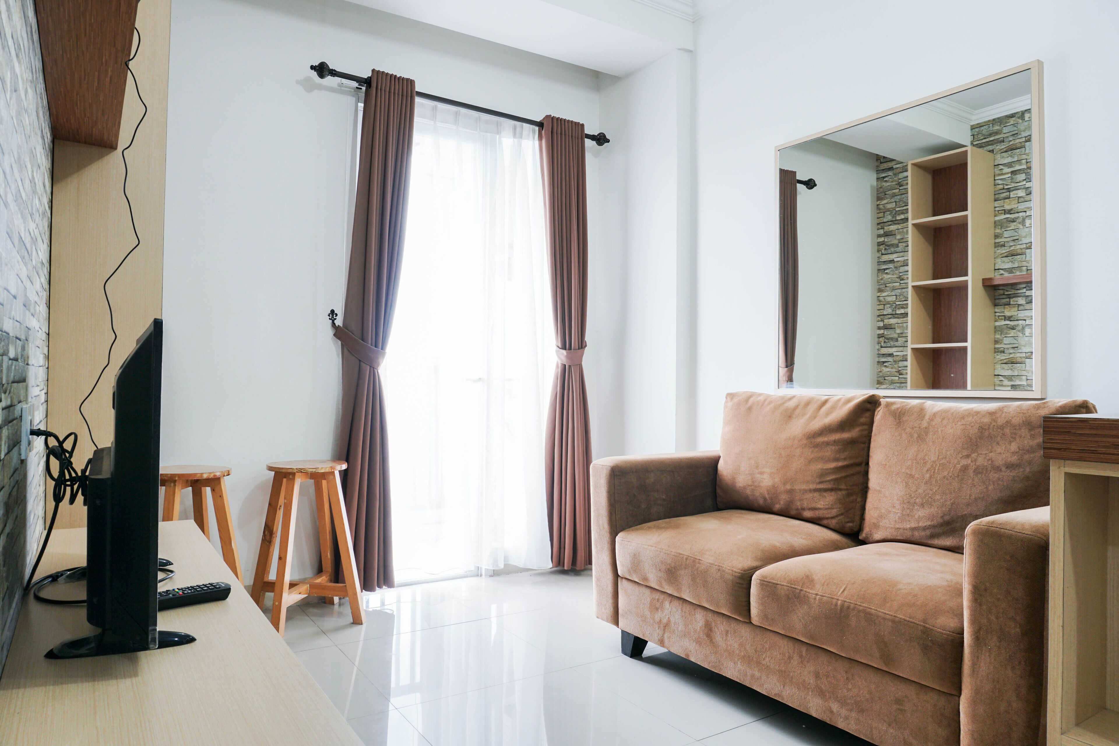 Una sala de estar con sofá, televisión, taburetes de madera y un espejo grande.