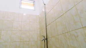 Un baño con azulejos color beige, un cabezal de ducha y una ventana con persianas.