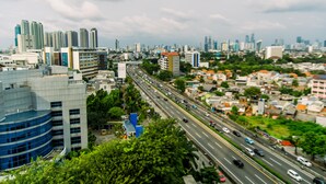 Un paisaje urbano con modernos rascacielos, una concurrida avenida de múltiples carriles y zonas verdes circundantes.