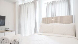 A hotel room with a neatly made bed, a bedside table with a radio, and a window with curtains. - Comfy And Nice Studio Apartment At Citra Living (Jakarta)