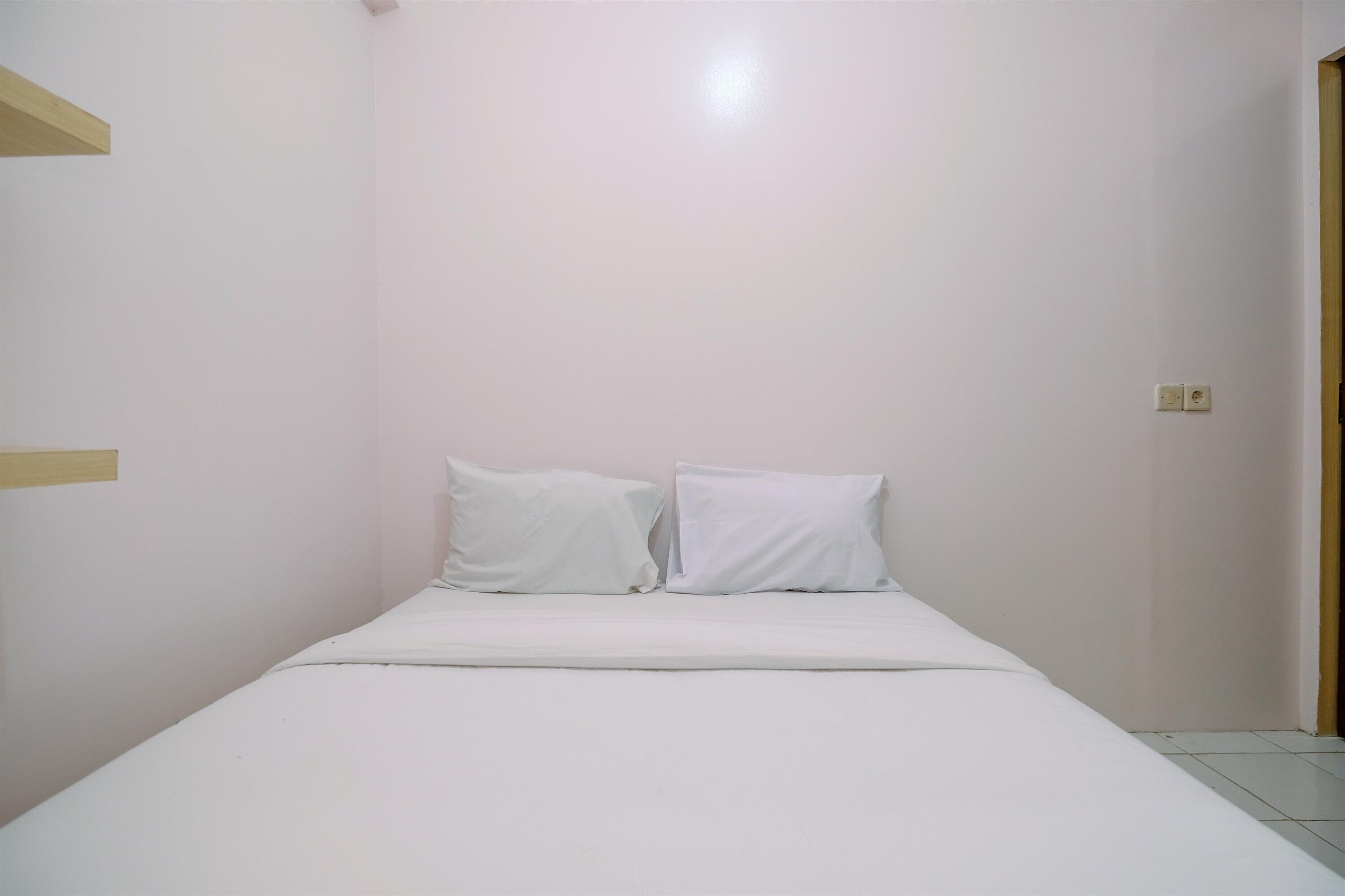 Una habitación pequeña y limpia con una cama individual, paredes blancas y una puerta de madera.