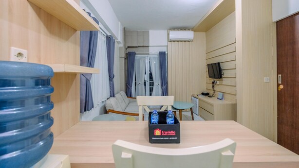 Una habitación de hotel compacta con piso de madera, una mesa de comedor con sillas, un sofá, un televisor sobre un mueble bajo y un dispensador de agua.