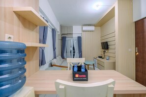 Une chambre d’hôtel compacte avec un plancher en bois, une table à manger avec des chaises, un canapé, un téléviseur posé sur un meuble et un distributeur d’eau.
