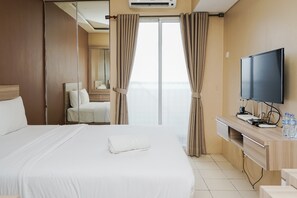 A hotel room with a large bed, a desk with a flat-screen TV, and a view of the city through the window.