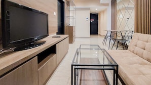 A modern living room with a flat-screen TV, glass coffee table, and beige sofa. - Nice And Comfort 1Br At Branz Bsd City Apartment (Pagedangan)