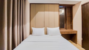 A bedroom with a bed, two pillows, a wooden bench, and a wardrobe. - Nice And Comfort 1Br At Branz Bsd City Apartment (Pagedangan)