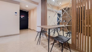 A modern hotel room with a wooden partition, a small table with four chairs, and a door with a fire exit sign. - Nice And Comfort 1Br At Branz Bsd City Apartment (Pagedangan)