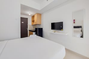 A hotel room with a bed, a television, a mirror, and a small shelf with a remote control. - Modern And Tidy Studio Serpong Garden Apartment (Cisauk)