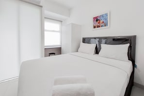 A modern bedroom with a large bed, a grey headboard, white bedding, and a small table with a chair. - Modern And Tidy Studio Serpong Garden Apartment (Cisauk)
