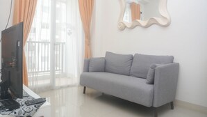 A living room with a grey sofa, a television, and a mirror on the wall. - Cozy And Tidy 2Br At Signature Park Grande Apartment (Jakarta)
