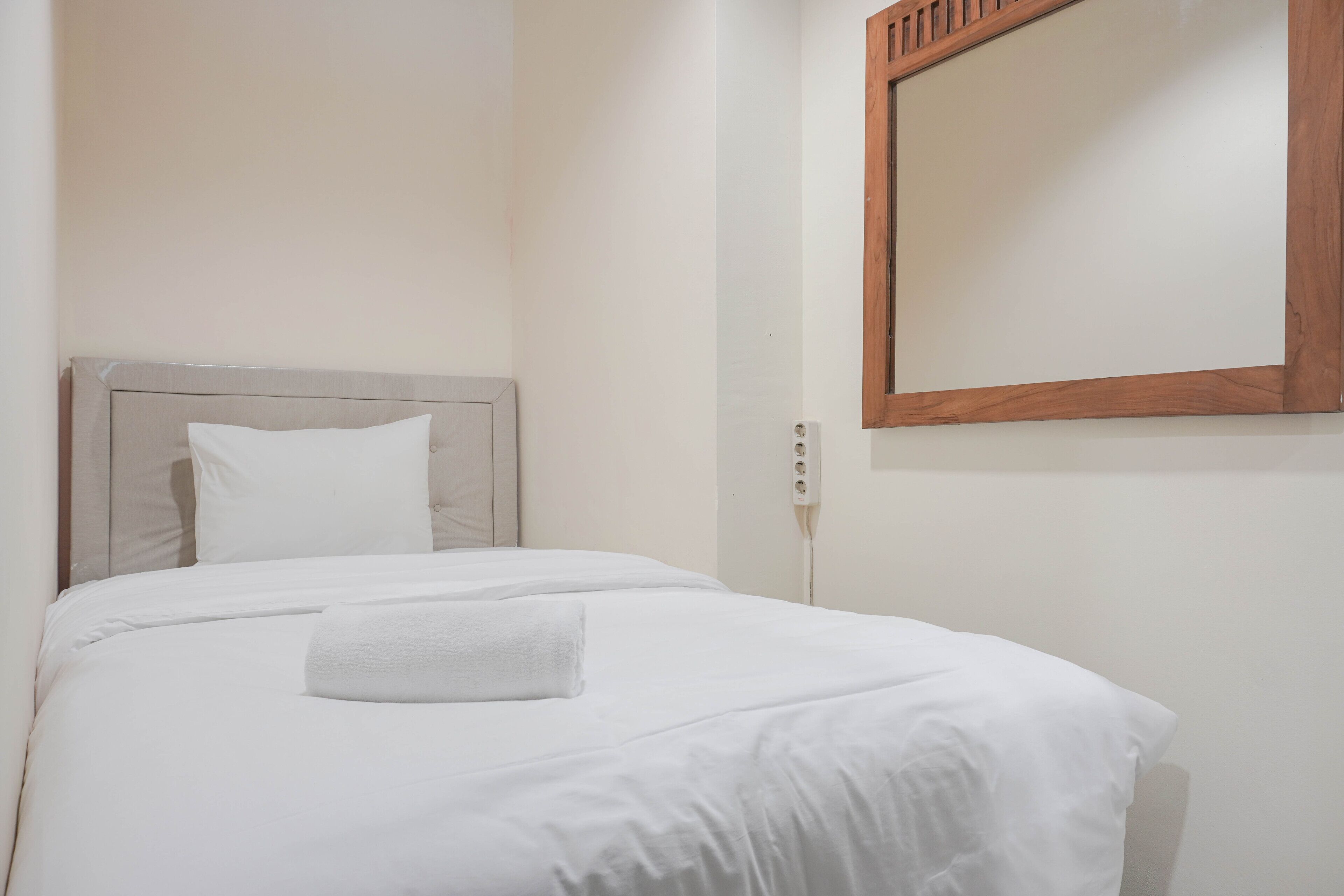 A neatly made bed with white linens and a single white pillow.