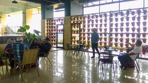 A spacious indoor area with a high ceiling, large windows, and a wall of hanging potted plants. - Comfort 1Br Apartment At Atlanta Residences (Depok)