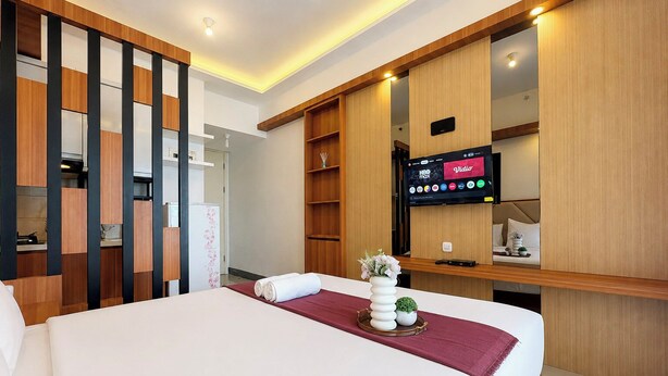 Una habitación de hotel con una cama, un televisor montado en la pared y un separador de madera.