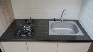 A kitchen with a black countertop, a stainless steel sink, and a gas stove. - Comfort And Homey Studio At Transpark Bintaro Apartment (Caringin)