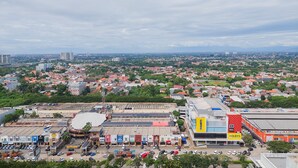 A cityscape with a prominent building featuring a yellow 'Courts' sign, surrounded by parked cars and greenery. - Comfort And Homey Studio At Transpark Bintaro Apartment (Caringin)