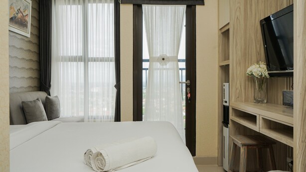 A hotel room with a bed, a TV, a desk, and a balcony view. - Comfort And Homey Studio At Transpark Bintaro Apartment (Caringin)