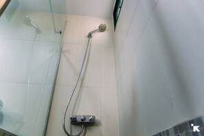 En duschhörna med glasväggar, ett duschmunstycke som kan hållas i handen och en väggmonterad kontrollpanel.