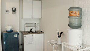 A kitchen with white cabinets, a blue refrigerator, a water dispenser, and a small sink. - Warm And Cozy Studio At Grand Kamala Lagoon Apartment (Bekasi)