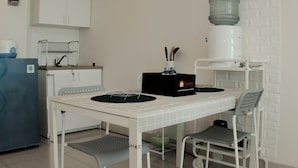 A small kitchenette with a white table, two chairs, a water dispenser, a coffee maker, and a small refrigerator. - Warm And Cozy Studio At Grand Kamala Lagoon Apartment (Bekasi)