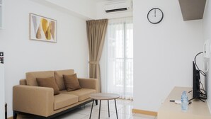 A modern living room with a beige sofa, a small round table, and a TV on a stand. - Nice And Fresh 2Br Apartment At M-Town Residence (Gading Serpong)
