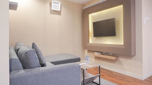 Un salon moderne avec un canapé gris, une petite table basse et un téléviseur à écran plat fixé au mur.