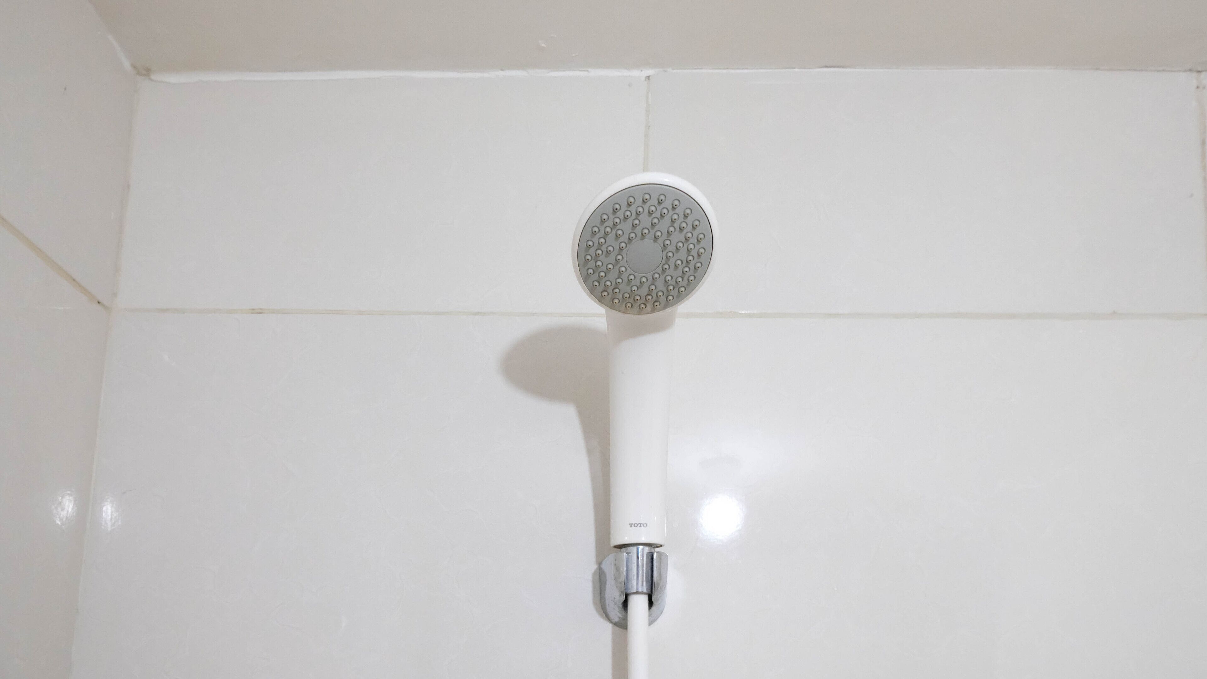 Un pommeau de douche fixé sur un mur recouvert de carreaux blancs.