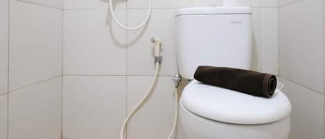 Eine weiße Toilette mit einem braunen Handtuch darauf, einem Toilettenpapierhalter und einem Duschschlauch.