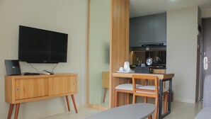 Ein modernes Hotelzimmer mit Flachbildfernseher, Holzmöbeln, einem Esstisch und einer Küchenzeile.