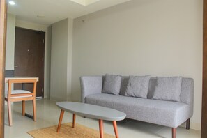 A living room with a grey sofa, a wooden chair, and a small table. - Wonderful 1Br Apartment At Mustika Golf Residence (Cikarang)