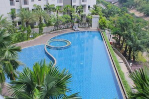 A large swimming pool surrounded by lush greenery and a multi-story building. - Wonderful 1Br Apartment At Mustika Golf Residence (Cikarang)