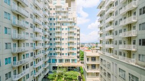Um edifício residencial com vários andares, varandas, um pátio central com vegetação e céu claro.