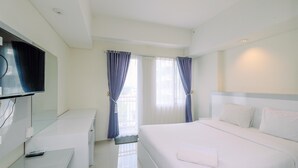 Quarto de hotel com cama, escrivaninha, televisão e cortinas.