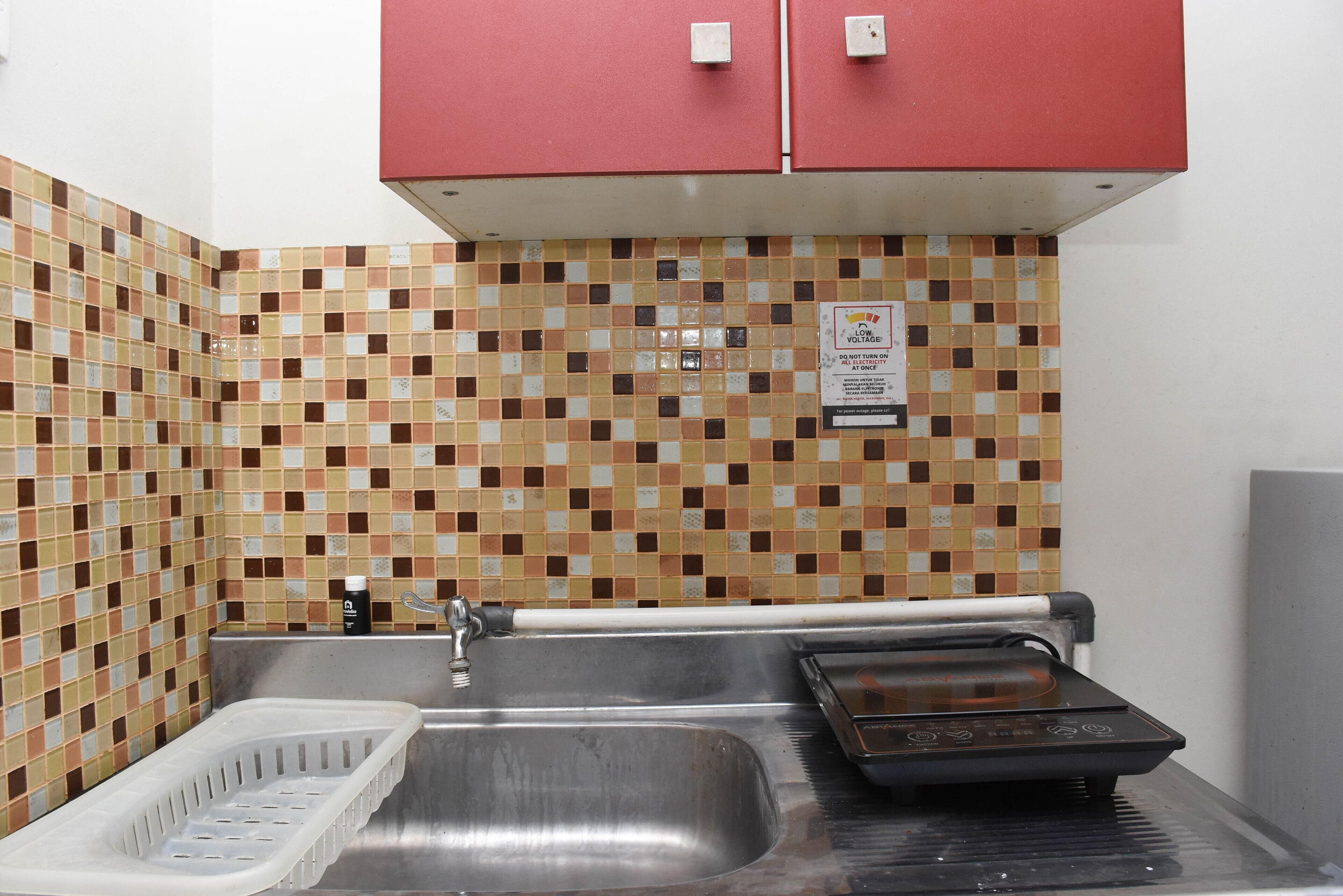 Een keuken met een roestvrijstalen spoelbak, een rode kast en een betegelde achterwand.