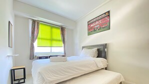Una habitación de hotel con cama, una ventana con cortinas, un cuadro enmarcado en la pared y una mesita.