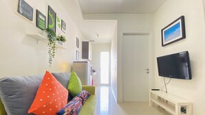 Una sala de estar con un sofá verde, cojines coloridos, un televisor de pantalla plana y un banco blanco.