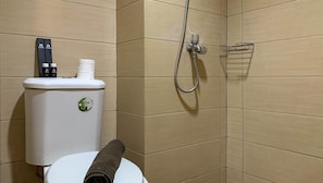 A bathroom with a toilet, a shower, and a towel rolled up on the floor. - Comfort And Homey Studio At Margonda Residence 5 Apartment (Depok)