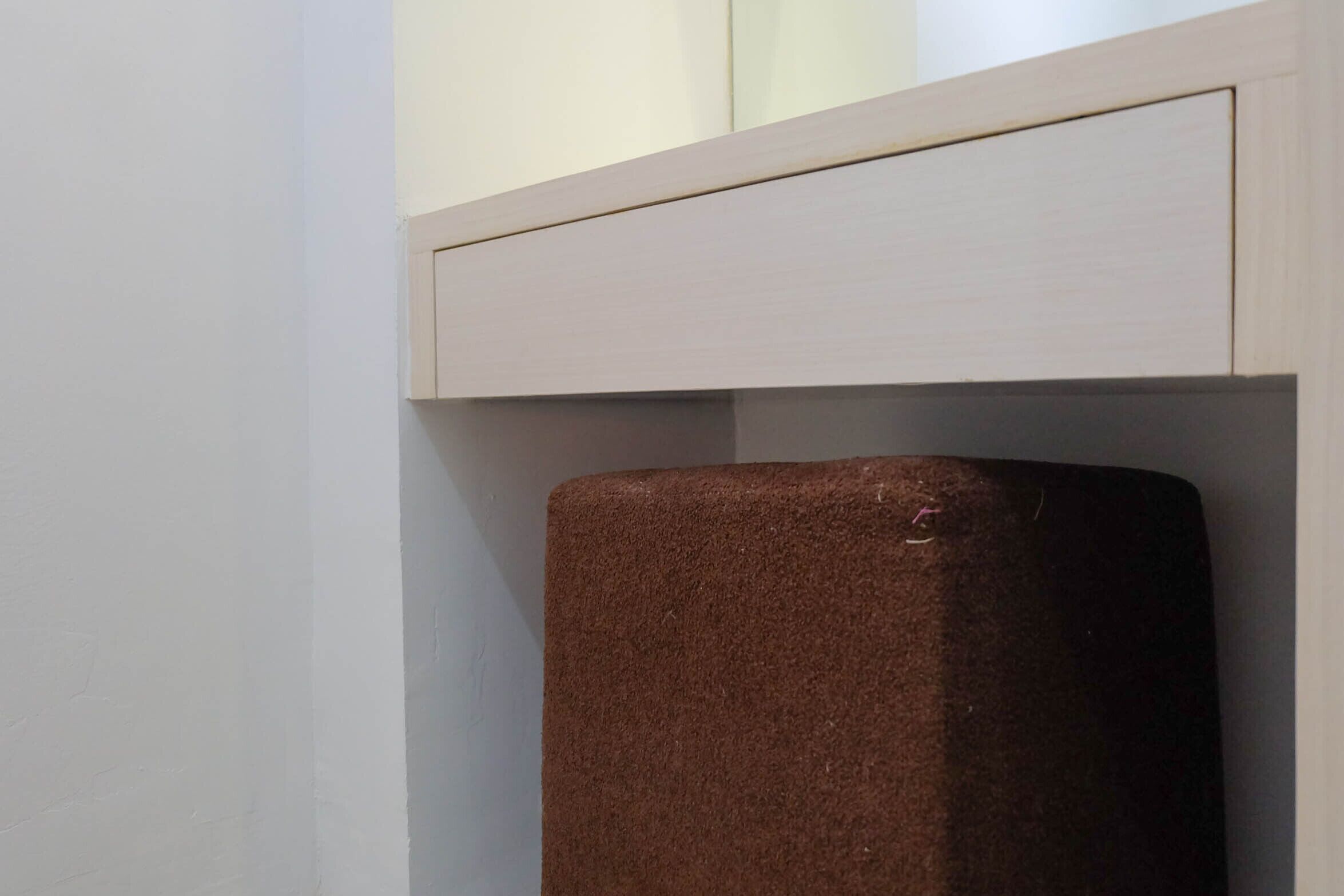 A corner of a room with a white wall and a brown object, possibly a piece of furniture or equipment, partially visible under a cabinet.