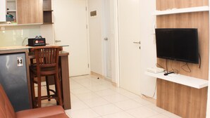 Un espace de vie compact comprenant un coin cuisine, un coin repas avec une chaise, un téléviseur fixé à un mur en bois et un petit réfrigérateur.