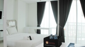 A hotel room with a bed, a bedside table with a minibar, and a window with curtains. - Best Choice and Comfy Studio Apartment LRT City Bekasi (Bekasi)