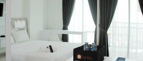 A hotel room with a bed, a bedside table with a minibar, and a window with curtains.