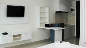 A modern kitchen with a built-in microwave, a flat-screen TV, and a small island with a sink. - Best Choice and Comfy Studio Apartment LRT City Bekasi (Bekasi)