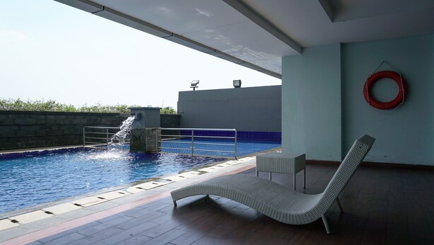 An indoor swimming pool with a lounge chair and a red lifebuoy on the wall. - Cozy Living Studio Apartment At Belmont Residence Near Puri (Jakarta)