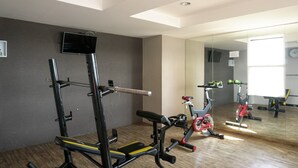 A gym with a weight bench, a squat rack, and an exercise bike. - Cozy Living Studio Apartment At Belmont Residence Near Puri (Jakarta)