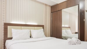 A neatly made bed with white linens, a wooden headboard, and a large mirror on the wall. - Cozy Living Studio Apartment At Belmont Residence Near Puri (Jakarta)