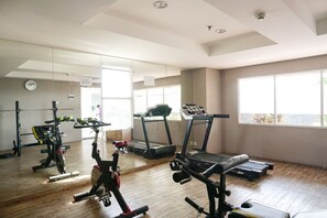 A gym with exercise equipment, large windows, and a mirror. - Cozy Living Studio Apartment At Belmont Residence Near Puri (Jakarta)