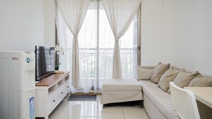 A modern, well-lit room with a sofa, a television, and a refrigerator. - Cozy Living 1Br At M-Town Signature Apartment (Gading Serpong)