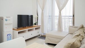 A modern living room with a flat-screen TV on a wooden TV stand, a white sofa, and a water dispenser. - Cozy Living 1Br At M-Town Signature Apartment (Gading Serpong)