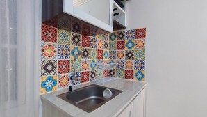 Una cocina con un lavamanos, un armario blanco y un salpicadero de azulejos de colores.