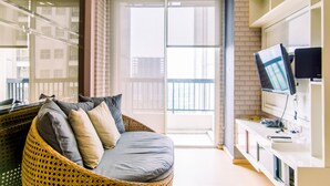 A modern living room with a wicker sofa, a flat-screen TV, and a sliding glass door leading to a balcony. - Warm And Comfort Stay 1Br Apartment At Silkwood Residences (Tangerang)